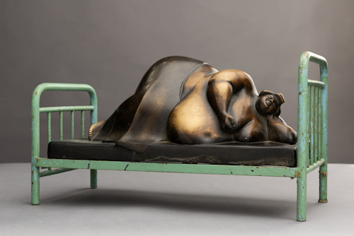 Bronze statue of an overweight person lying on a bed