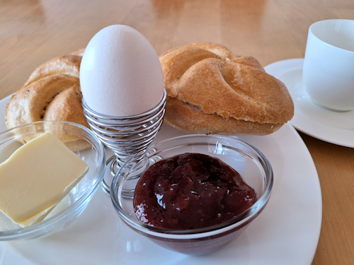 Two rolls, an egg, butter and jam on a plate